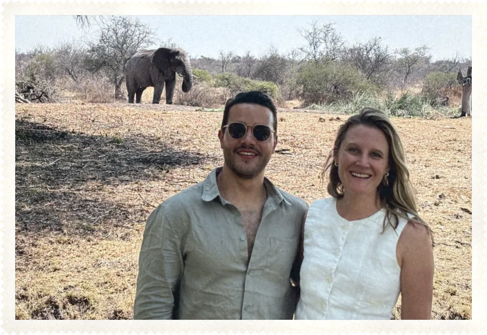 Katie and Carlos on safari, with an elephant behind them